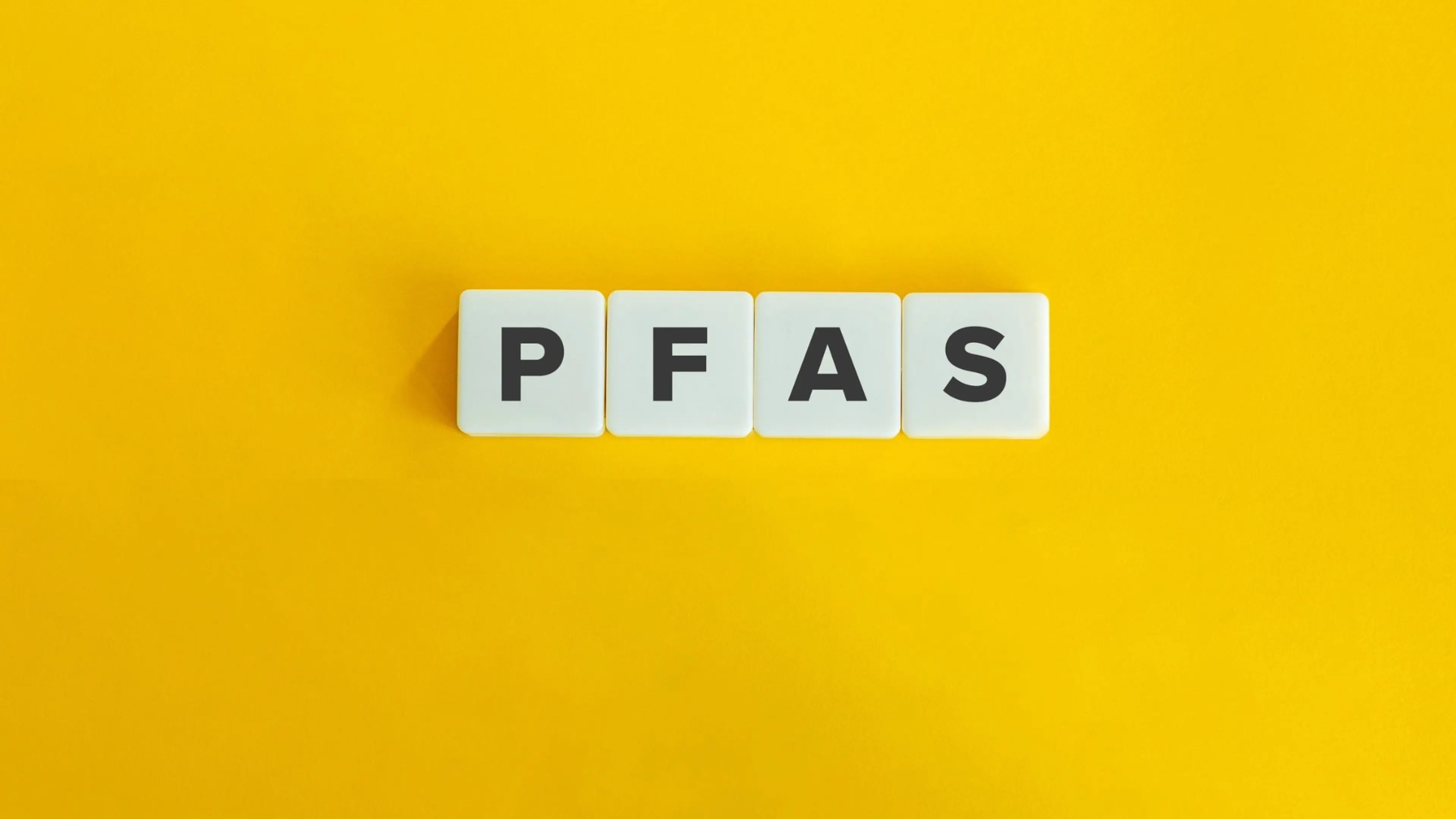 wooden letter blocks spelling PFAS on bright yellow background